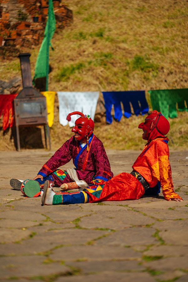 Two atsaras in red masks lounging on the courtyard flagstones between acts