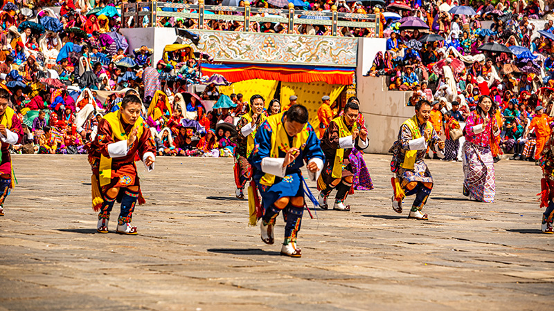 Dancers in traditional gho and kira before packed festival stands at Thimphu Tshechu